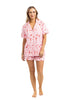 A woman stands barefoot against a white background wearing Katydids Literally Just A Girl Icons Short Pajama Set—light pink, short-sleeve button-up shirt and matching shorts, both adorned with a cute red bow print.