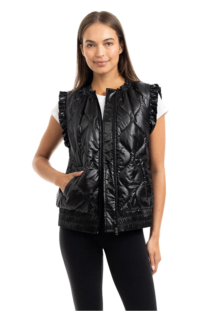 A woman models the Katydid Black Metallic Quilted Vest over a white top and black leggings, smiling softly against a plain white background—highlighting this shiny womens fall outerwear piece.