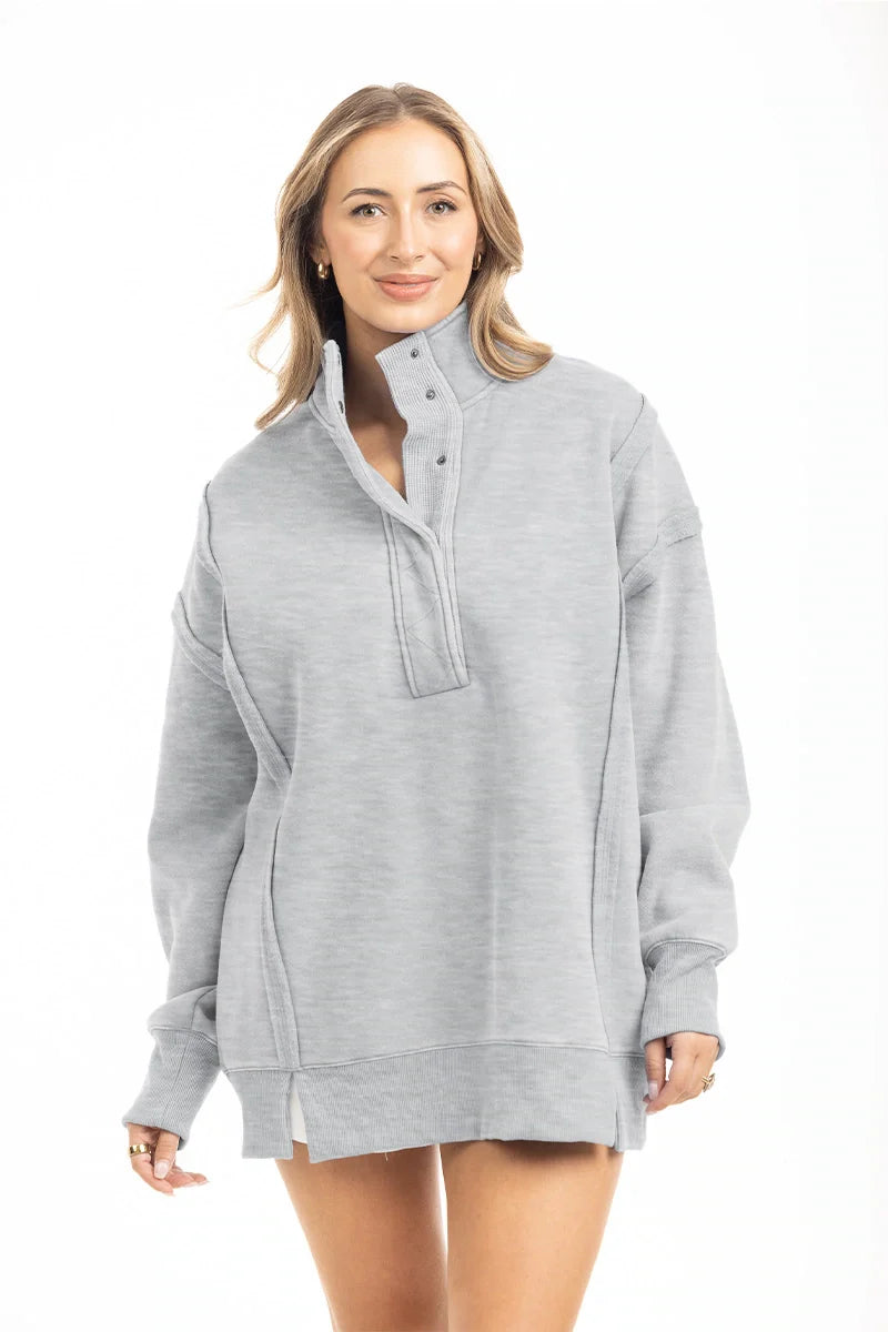 A woman with light brown hair smiles gently at the camera, wearing the Katydid Gray Vintage Wash Pullover Jacket featuring an oversized fit, snap-neck collar, long sleeves, and side slits against a white background.