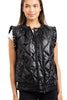 A woman wears the Katydid Black Metallic Quilted Vest with ruffled cap sleeves and a front zipper over a white short-sleeve top, standing and smiling—a stylish fall layer for women.