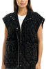 A woman wears the Katydid Charcoal Oversized Garment Washed Quilted Vest, featuring large pockets and a tie detail, over a white shirt while standing against a plain white background.
