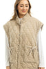 A woman with light brown hair smiles with her eyes closed, wearing the Katydid Beige Oversized Garment Washed Vest featuring snap buttons and two large front pockets tied with bows over a long-sleeve white top.