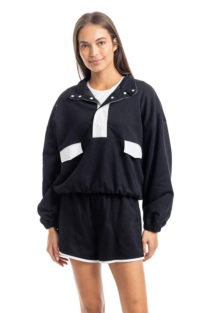 A woman faces forward in the Katydid Black  White Quarter Snap Athletic Set for women, featuring a loose pullover and matching shorts. She smiles softly, with straight hair, against a plain white background.