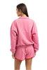 A woman with straight brown hair models the Katydid Pink  Orange Quarter Snap 2 Piece Athletic Set—vibrant loungewear in ultra-soft performance fabric. She faces away from the camera, her left hand resting at her side.