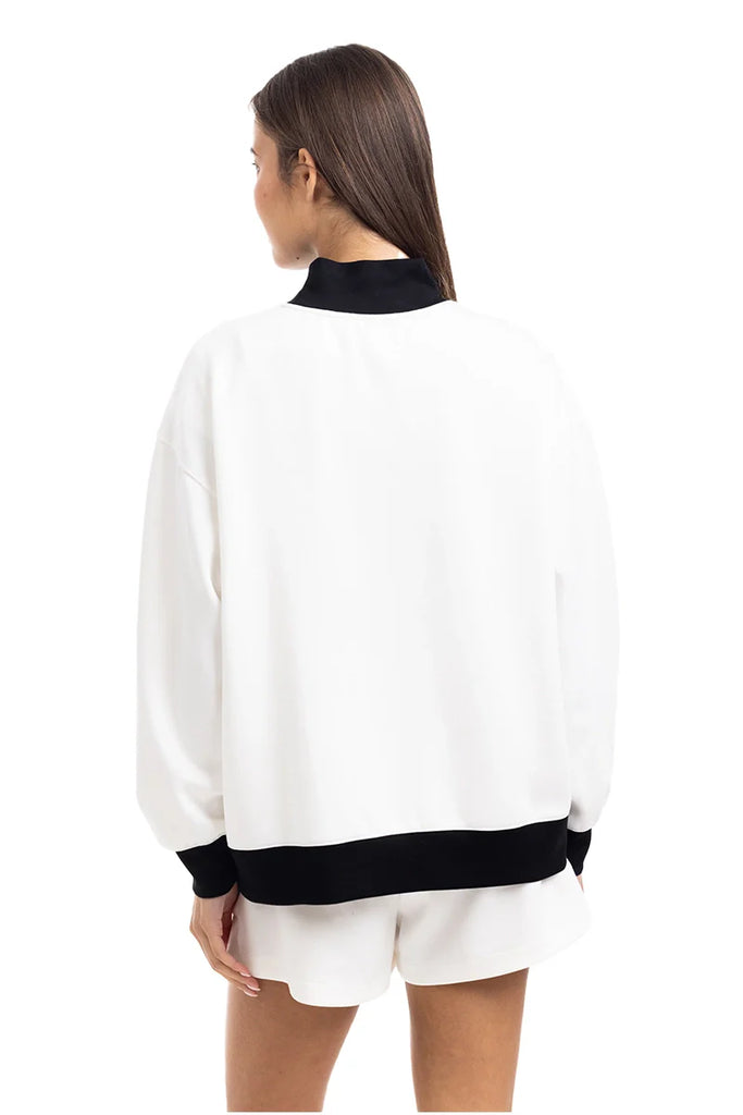 A woman with long brown hair is seen from the back wearing the Katydid White  Black Duo Mockneck Set—featuring a loose white jacket with black accents and matching shorts—against a plain white background.