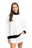 A woman in the Katydid White  Black Duo Mockneck Set—featuring a mockneck top with black collar and cuffs and matching white shorts—stands smiling with one hand in her pocket against a plain white background.