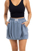Woman wearing the Katydid Steel Blue Mini Bubble Skirt with pockets and a visible Katydid label on the waistband, paired with a black sleeveless crop top and bracelets on her left wrist.