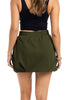A woman with wavy brown hair is seen from the back wearing a black sleeveless crop top and the Katydid Olive Athletic Skirt for Women, featuring an elastic waistband, paired with bracelets on her wrists.