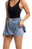 A woman wearing a black sleeveless top and the Katydid Steel Blue Mini Bubble Skirt holds up its blue skirt-like layer to reveal fitted shorts with pockets underneath.
