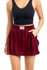 A woman wears the Katydid Wine Bubble Skirt Skort, featuring pockets and an elastic waistband. She pairs it with a sleeveless black crop top—her left hand in a pocket, bracelets on her right wrist—making it a perfect fall outfit.
