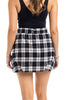 A woman is seen from behind wearing the Katydid Black Autumn Plaid Skirt with Shorts and a black tank top, accessorized with bracelets on her right wrist for a chic fall look.