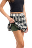 A person in a black top lifts a Green Autumn Plaid Skort by Katydid to reveal matching green shorts underneath. The background is white.