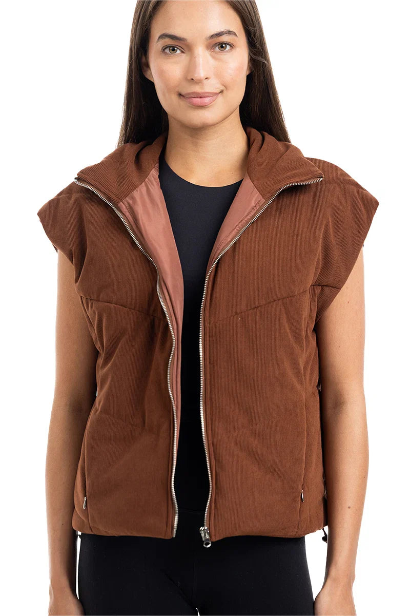 A woman models the Katydid Brown Corduroy Quilted Vest over a black top, standing against a white background—a stylish and effortless fall fashion look.
