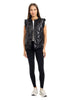 A woman faces forward against a white background, wearing the Katydid Black Metallic Quilted Vest with ruffled shoulders over a white top, paired with black leggings and white sneakers—an ideal women’s fall layer.