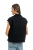 A person with long brown hair stands facing away from the camera in light blue jeans and a Katydid Black Corduroy Trendy Puffer Vest against a white background.