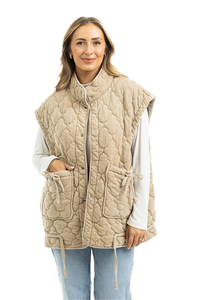 A woman wears the Katydid Beige Oversized Garment Washed Vest over a white long-sleeve top and light blue jeans, smiling while standing against a plain white background.