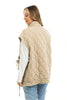 A woman wears the Katydid Beige Oversized Garment Washed Vest, featuring a diamond-quilted texture and side tie detail, layered over a white long-sleeve shirt and blue jeans. She stands facing slightly away against a plain white background.