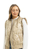 A woman smiles with her eyes closed against a white background, modeling the Katydid Soft Tan Metallic Quilted Vest with ruffled shoulders over a white long-sleeve shirt, highlighting the vest’s stylish charm.