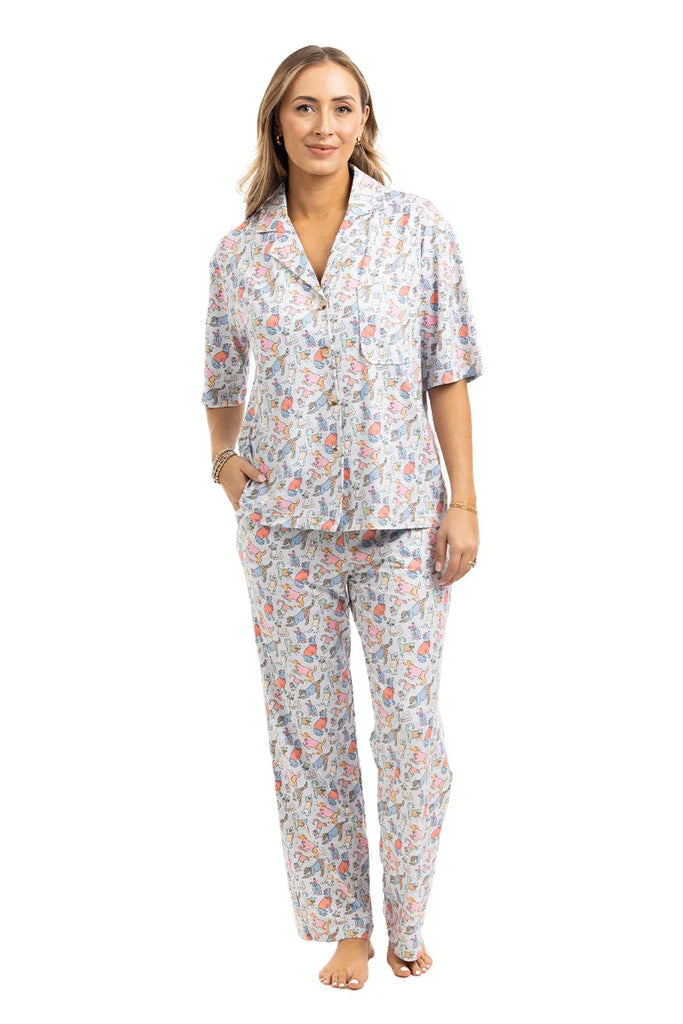 A woman smiles with her hands in her pockets, wearing Katydids Posh Pets Preppy Pajama Pants featuring a colorful floral print. The comfy, pet lover design is perfect for animal enthusiasts, shown here barefoot against a white background.