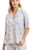 A woman with light brown hair, smiling softly, models the Katydid Posh Pets Preppy Pajama Pants—a colorful, playful animal print sleepwear perfect for pet lovers. She wears the matching short-sleeve button-up top with her hand at her side.