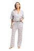 A woman with light brown hair and a relaxed expression stands barefoot in Katydid’s Posh Pets Preppy Pajama Pants—a colorful floral, pet lover set featuring a short-sleeve button-up top and drawstring pants, perfect for animal enthusiasts.
