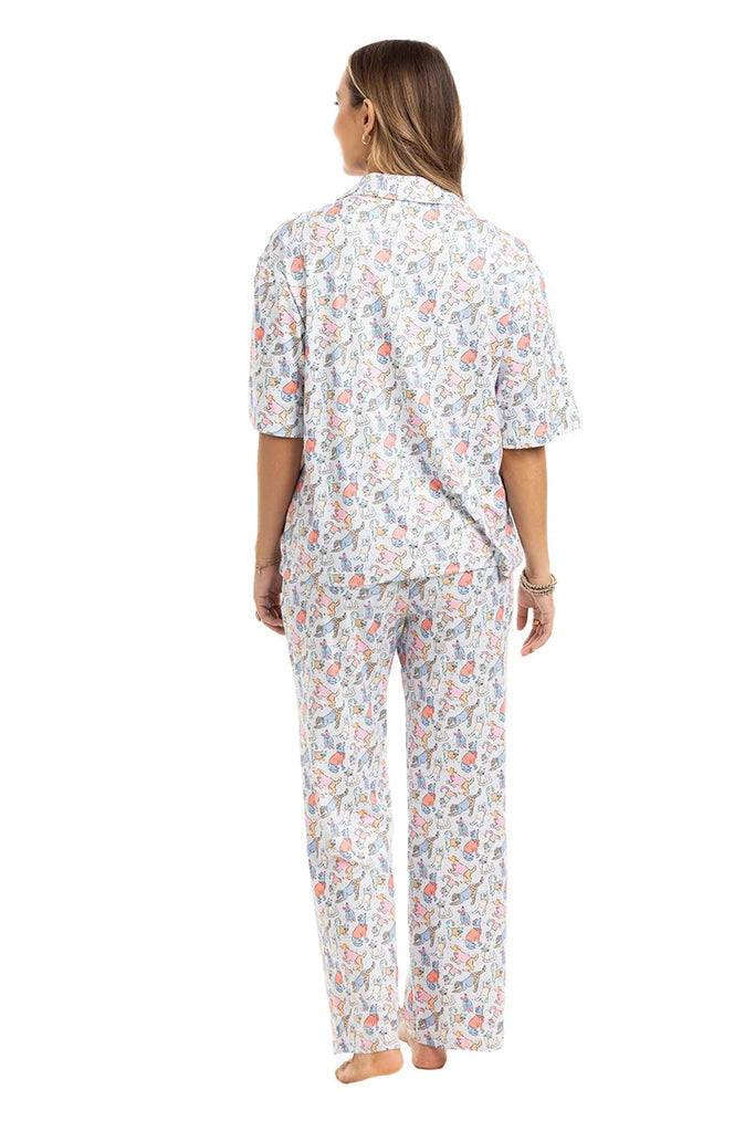 A woman stands barefoot, facing away, wearing Katydids Posh Pets Preppy Pajama Pants with a colorful floral pattern on white. This animal lover’s pajama set includes a short-sleeve top and full-length pants. The background is plain white.