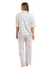A woman stands barefoot, facing away, wearing Katydids Posh Pets Preppy Pajama Pants with a colorful floral pattern on white. This animal lover’s pajama set includes a short-sleeve top and full-length pants. The background is plain white.