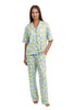 A woman wears the Katydid Zesty Lemons Matching Pajama Pants Set, featuring a light blue short-sleeve button-up shirt and long, loose pants with a bright yellow lemon print. She is barefoot and smiles slightly.