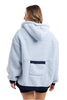 A person with shoulder-length hair is wearing the Katydid Light Blue Two-Toned Sherpa Fleece Pullover, featuring a cozy hood, dark blue trim, and a rectangular pocket on the lower back. They are facing away from the camera.
