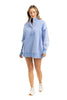 A woman in the Katydid Light Blue Vintage Wash Snap-Neck Pullover, styled with white sneakers, stands against a plain white background, smiling and looking down.