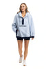 A woman in a Katydid Light Blue Two-Toned Sherpa Fleece Pullover with a front pocket, navy shorts, and white sneakers walks forward, smiling against a plain white background.