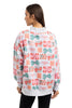 A woman with straight brown hair, seen from the back, wears the Katydid Wrapped Presents with Bows Mockneck Pullover, a festive holiday sweatshirt adorned with colorful gift boxes, paired with black pants.