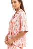 A woman stands sideways, smiling gently in the Katydid Womens Boots  Roses PJ Set—a cute, loose-fitting pajama with a colorful cowboy boot pattern and short sleeves for comfy cowgirl style.