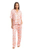 A woman smiles barefoot in the Katydid Womens Boots  Roses PJ Set—light pink with a colorful dog print. This set includes a button-up short-sleeve top and long pants, perfect playful cowgirl loungewear for relaxing at home.