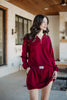 A woman with long, wavy brown hair wears the Katydid Wine Bubble Skirt Skort and a matching maroon zip-up sweatshirt, standing indoors by large windows with a relaxed expression.