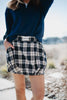 Outdoors, a woman wears a navy long-sleeve top and the Katydid Blue Autumn Plaid Skirt with pockets and built-in shorts. The skirt features a Katydid label on the waistband, and she tucks her hand into one pocket.