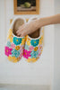 A hand holds the Katydid Spring Flowers House Slippers for Women, featuring colorful blue, pink, and yellow floral patterns, against a light indoor background.
