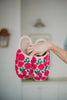 A hand displays Katydid’s Whimsical Roses Fuzzy Slippers for women, featuring bright pink embroidered roses and green leaves, against a softly blurred indoor background.