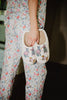 Wearing pastel animal-print pajamas, a woman holds Katydid’s Posh Pets Women Slippers—fuzzy sherpa footwear featuring cute, colorfully dressed animals—for a cozy, relaxed vibe indoors.