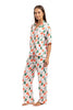 A woman stands barefoot in Katydids Santas Mail Christmas Pajamas for Women, a festive matching set featuring a red, green, and white gift box pattern with a button-up short-sleeve top and long pajama pants.