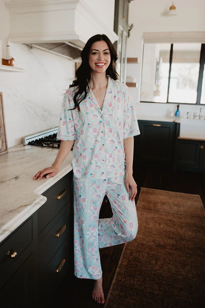 A woman in Katydids Mahjong Pieces Pajama Pants Set stands barefoot in a modern kitchen, smiling at the camera with one hand on the counter.