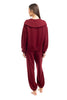 A woman with long brown hair, barefoot and facing away, showcases the Katydid Wine Pants Two-Piece Set with a cozy maroon wide-collar sweatshirt and matching pants against a plain white background.