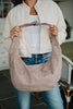 A woman in a cream jacket, white top, and jeans holds the Katydid Khaki Lightweight Suede Tote Bag with both hands. The photo, cropped above her nose, highlights the stylish bag and her chic outfit.