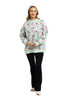A woman smiles, wearing the Katydid Holiday Champagne, Coupes  Holly Mockneck Sweatshirt with a festive print, paired with black pants and white sneakers against a white background.