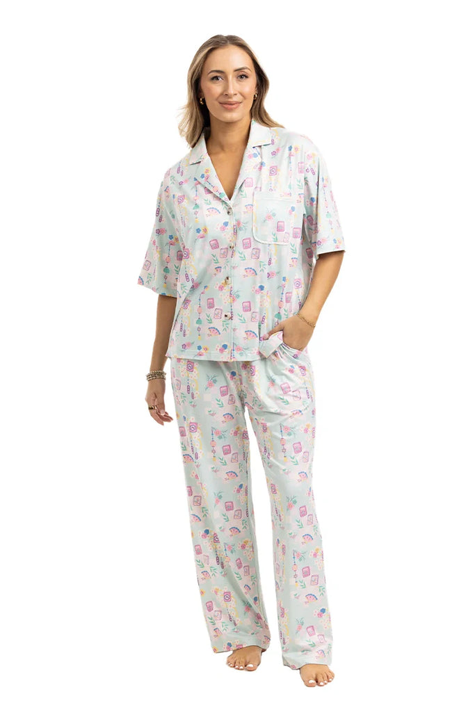 A woman models the Katydid Mahjong Pieces Pajama Pants Set: a light-colored, short-sleeve button-up shirt with matching long pants, featuring a playful print—ideal for fans of girly pajamas.