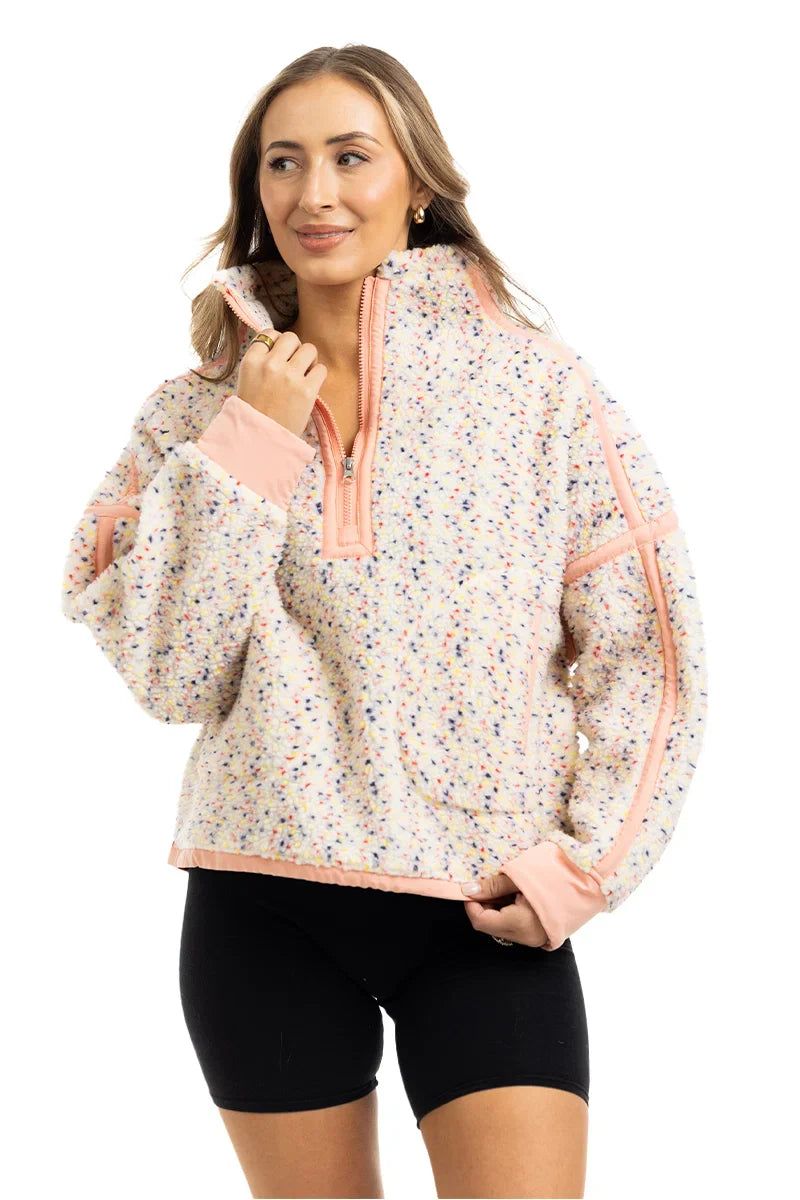 A woman models the Katydid Confetti Print Womens Pullover with a half-zip collar and peach trim, paired with black shorts, standing against a white background and smiling slightly.