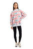 A woman faces forward against a plain white background, wearing the Katydid Wrapped Presents with Bows Mockneck Pullover, featuring a festive pink, red, and green gift box pattern, paired with black leggings and white sneakers.