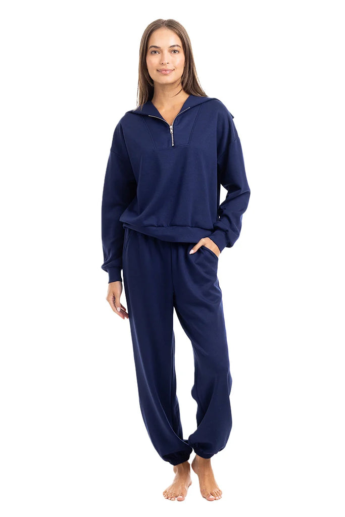 A woman stands barefoot, modeling the Katydid Classic Navy Two-Piece Pants Set with a half-zip pullover and relaxed-fit pants against a plain white background.