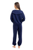 A woman with long brown hair stands barefoot, facing away, modeling the Katydid Classic Navy Two-Piece Pants Set with a wide-collar long-sleeve top and elastic cuff pants, set against a white background.
