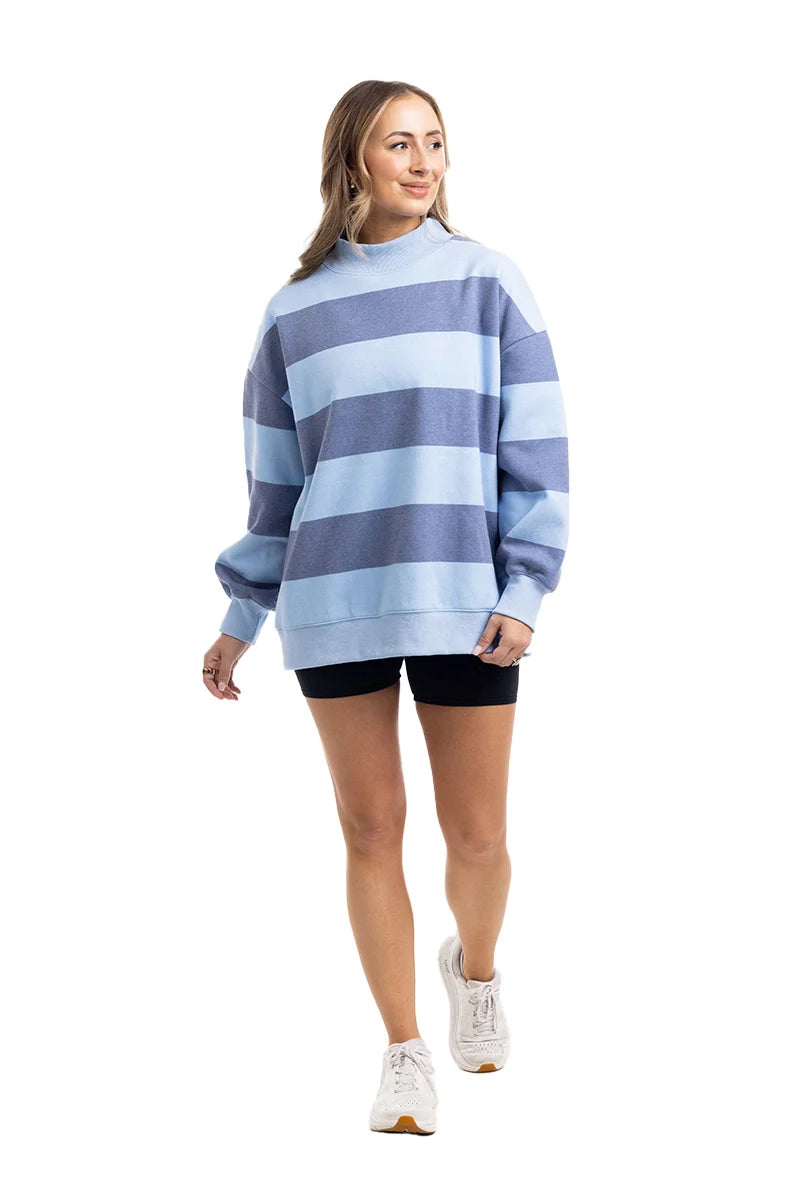 A woman stands and smiles against a white background in the Katydid Light Blue and Navy Striped Mockneck Sweatshirt—an effortless layering piece for fall.